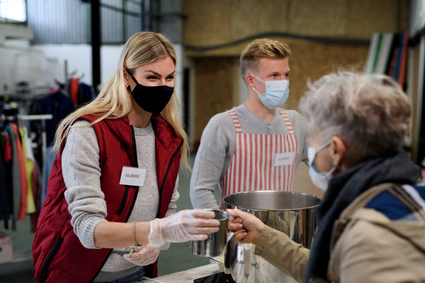 Volunteers serving hot soup for homeless in community charity donation center, coronavirus concept. - Foto, afbeelding