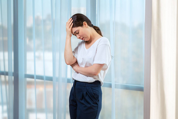 Eine junge, traurige Frau hält ihren Kopf mit der Hand und weint. Im Hintergrund des Fensters. Das Konzept der häuslichen Gewalt. - Foto, Bild