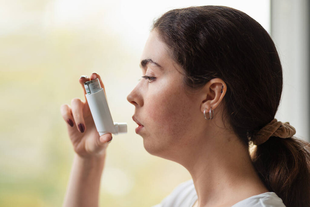 Close-up portret van een jonge vrouw die een inhalator tegen haar mond houdt. Zijaanzicht. - Foto, afbeelding