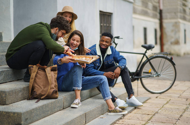 Group of young people outdoors in town, eating pizza. Coronavirus concept. - Фото, изображение