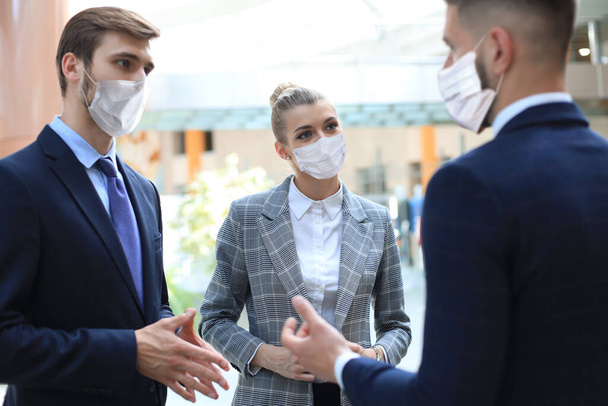 Three young businessmen wear preventive masks during epidemy, stand and discuss business at an office meeting. - Photo, Image
