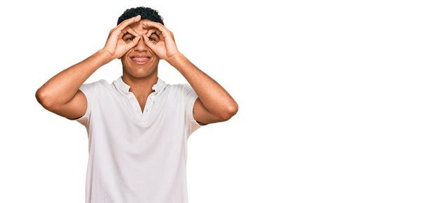 Jonge Arabier man draagt casual kleding doet ok gebaar als verrekijker steken tong uit, ogen kijken door vingers. gekke uitdrukking.  - Foto, afbeelding