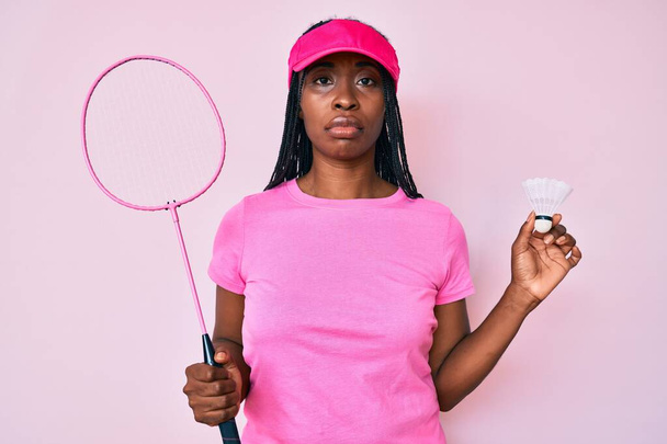 Femme afro-américaine avec des tresses tenant raquette de badminton détendue avec une expression sérieuse sur le visage. simple et naturel regardant la caméra.  - Photo, image