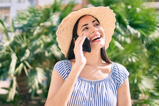 jong latin toeristisch meisje op vakantie glimlachend gelukkig praten op de smartphone in de stad. - Foto, afbeelding