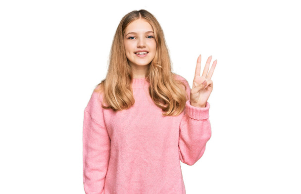 Kaunis nuori valkoihoinen tyttö yllään rento talvi villapaita näyttää ja osoittaa sormilla numero kolme hymyillen itsevarma ja onnellinen..  - Valokuva, kuva