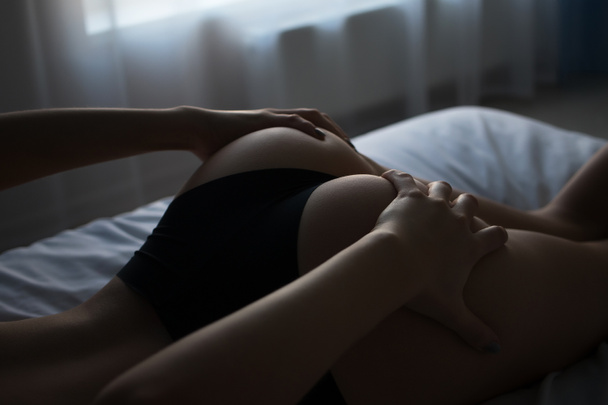 Πίσω όψη του λεπτού σεξουαλική γυμνή γυναίκα σε κιλότα που βρίσκονται στο κρεβάτι στο δωμάτιο - Φωτογραφία, εικόνα