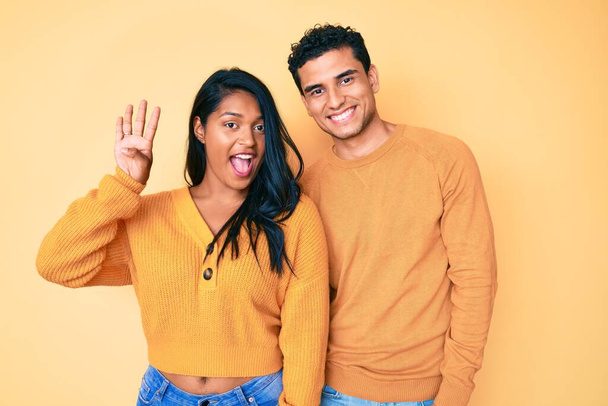 Krásný latinsky mladý pár na sobě ležérní oblečení spolu ukazuje a ukazuje s prsty číslo čtyři a zároveň se usmívá sebevědomě a šťastně.  - Fotografie, Obrázek