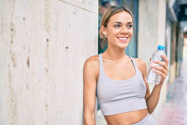 Joven cauciasiano fitness mujer usando deporte ropa entrenamiento al aire libre beber agua dulce - Foto, Imagen