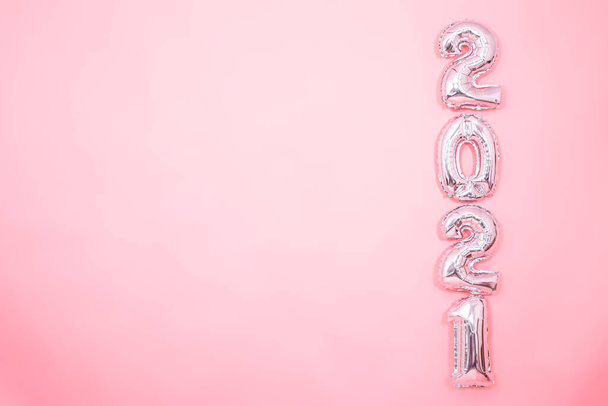 Lichtroze achtergrond met zilveren ballonnen in de vorm van cijfers 2021 aan de rechterkant, nieuwjaarsconcept - Foto, afbeelding