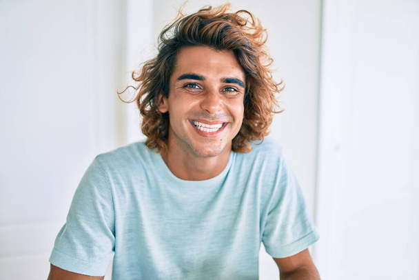 Young hispanic man smiling happy sitting on the table at home - Photo, Image
