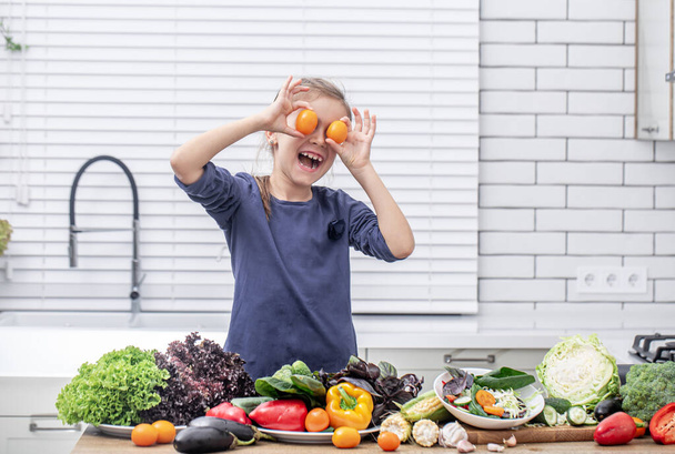 Милая маленькая девочка держит свежие овощи во время подготовки салата копировать пространство. - Фото, изображение
