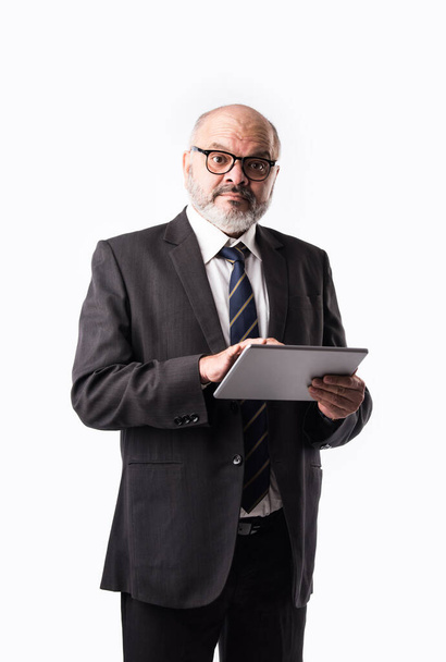Portrait of Senior Indian asian businessman using laptop, tablet or smartphone while standing against white background, showing or presenting - Fotoğraf, Görsel