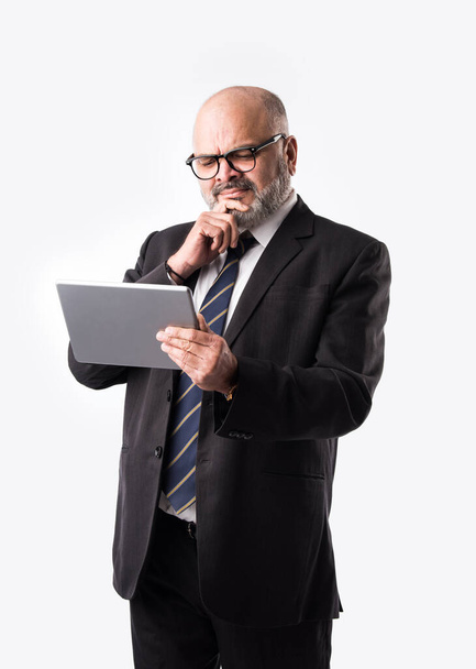 Portrait of Senior Indian asian businessman using laptop, tablet or smartphone while standing against white background, showing or presenting - Фото, изображение