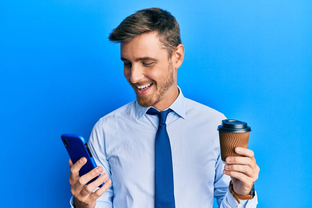 Όμορφος καυκάσιος επιχειρηματίας που χρησιμοποιεί smartphone και πίνει ένα φλιτζάνι καφέ χαμογελώντας και γελώντας δυνατά επειδή αστείο τρελό αστείο.  - Φωτογραφία, εικόνα