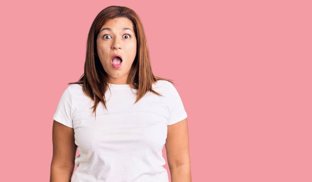 Middle age latin woman wearing casual white tshirt afraid and shocked with surprise and amazed expression, fear and excited face.  - Zdjęcie, obraz