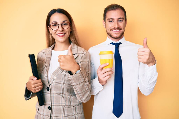 Beautiful couple wearing business clothes drinking take away coffee holding folder smiling happy and positive, thumb up doing excellent and approval sign  - Фото, зображення