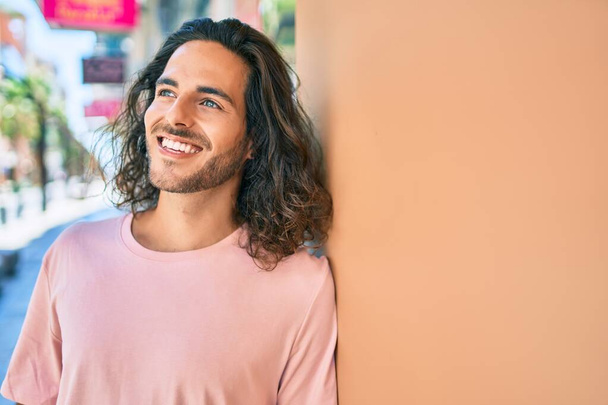 Young hispanic man smiling happy looking to the side leaning on the wall - Photo, image