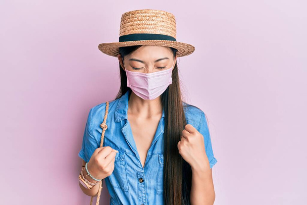 若いです中国人女性身に着けています医療マスク上の夏祝い驚きと腕を上げて成功のために驚いて目を閉じて  - 写真・画像