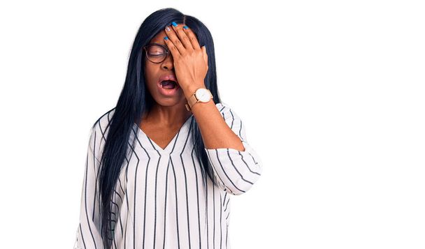 Молода афро-американська жінка в повсякденному одязі і окуляри позіхають, закриваючи половину обличчя, очі і рот рукою. Біль завдає болю.  - Фото, зображення