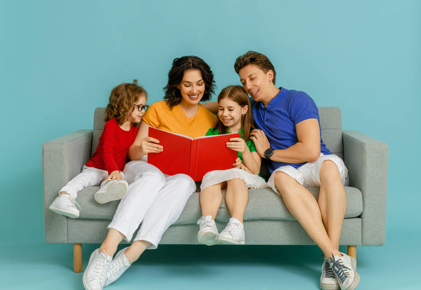 Happy loving family. Mother, father and children daughters reading a book on blue background.  - Foto, Imagem