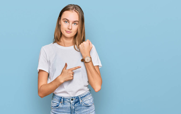 Beautiful young blonde woman wearing casual white t shirt in hurry pointing to watch time, impatience, looking at the camera with relaxed expression  - Φωτογραφία, εικόνα