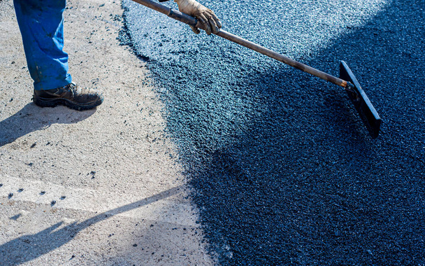 Trabajador regular la colocación de asfalto nuevo para parchear un bache en la carretera. - Foto, imagen