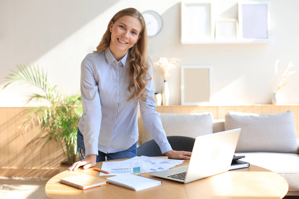 Confident young businesswoman with a friendly smile standing behind her desk in a home office - Foto, imagen