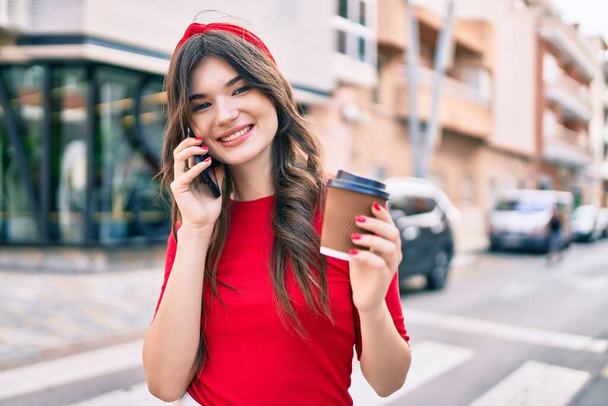 Young caucasian woman talking on the smartphone and drinking take away coffee at the city. - 写真・画像