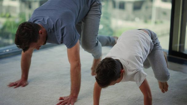 Sporty father and son training together. Dad and child doing workout at home. - Фото, зображення