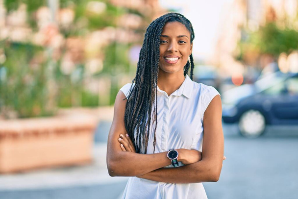 Fiatal afro-amerikai nő, keresztbe tett karokkal, boldogan mosolyog a városra.. - Fotó, kép