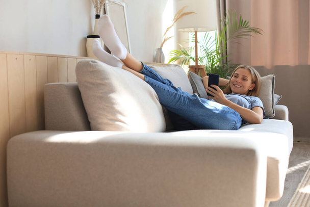 Pretty girl using her smartphone on couch at home in the living room - Fotó, kép