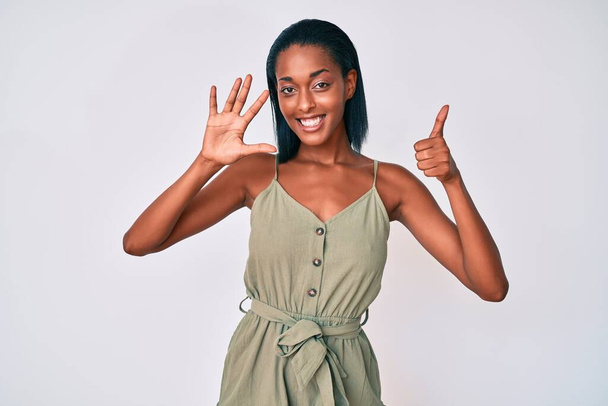 Молода афро-американська жінка в повсякденному одязі показує і вказує вгору з пальцями номер шість, посміхаючись впевнено і щасливо.  - Фото, зображення