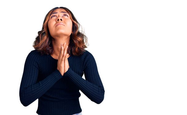 Jonge mooie gemengde ras vrouw dragen casual kleding bedelen en bidden met de handen samen met hoop uitdrukking op het gezicht zeer emotioneel en bezorgd. bedelen.  - Foto, afbeelding
