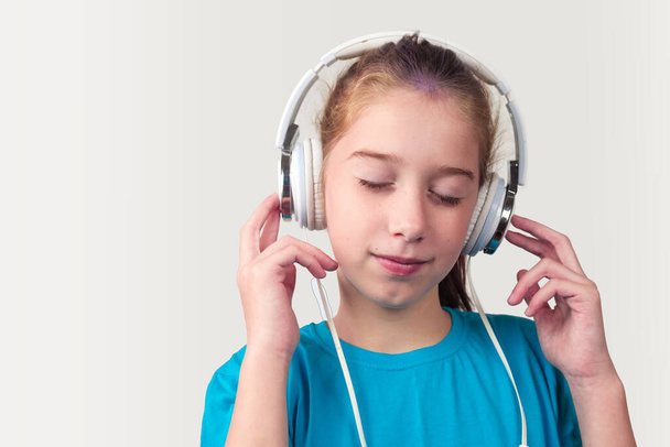 Mavi gömlekli bir kız kulaklık takıyor ve müzik dinliyor. - Fotoğraf, Görsel