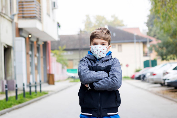 Portret van een zelfverzekerd kind dat een beschermend gezichtsmasker draagt terwijl hij op straat staat tijdens een coronavirus pandemie.  - Foto, afbeelding