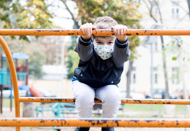 Niño feliz jugando en el patio de recreo y usando mascarilla debido a la pandemia de COVID-19.  - Foto, imagen