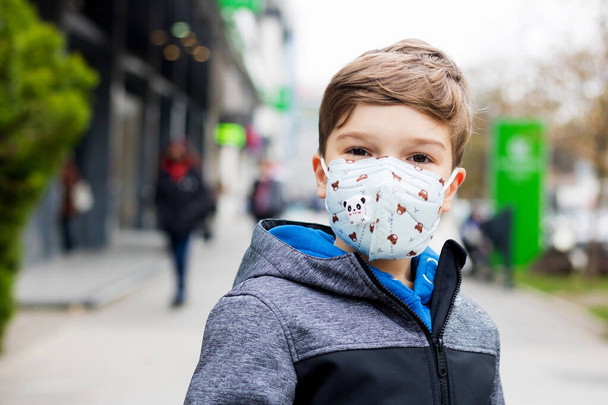 Muotokuva hymyilevä poika yllään suojaava kasvonaamio kävellessään kaupungin aikana COVID-19 pandemia.  - Valokuva, kuva