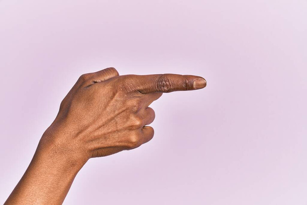 Braço e mão de mulher de meia-idade preta sobre fundo isolado rosa apontando com o dedo indicador para o lado, sugerindo e selecionando uma escolha  - Foto, Imagem