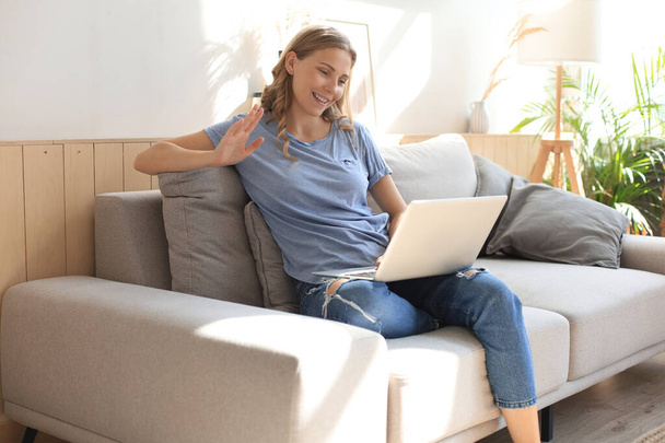 Smiling girl sit on couch watching webinar on laptop. Happy young woman study on online distant course - Photo, Image