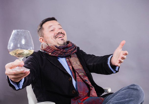 Solid cheerful man in kerchief sitting with glass of wine - Foto, Imagen
