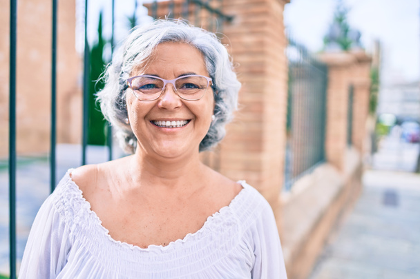 Femme d'âge moyen aux cheveux gris souriant heureux en plein air - Photo, image
