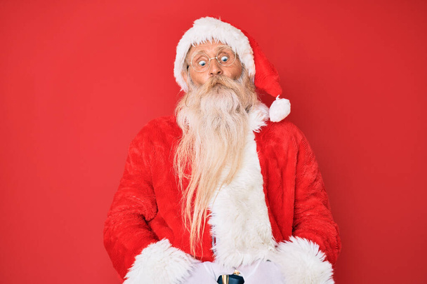 Old senior man with grey hair and long beard wearing traditional santa claus costume making fish face with lips, crazy and comical gesture. funny expression.  - Photo, Image