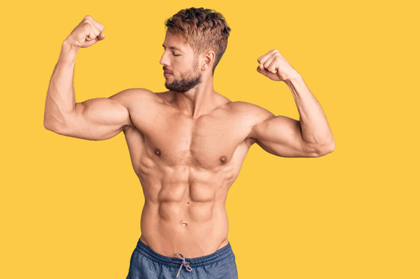Jeune homme caucasien debout torse nu montrant les muscles des bras souriant fier. concept de fitness.  - Photo, image