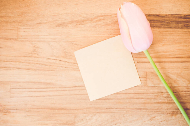 An overhead shot of a pink tulip flower and a blank sticky note on a wooden table with space for your text - Zdjęcie, obraz