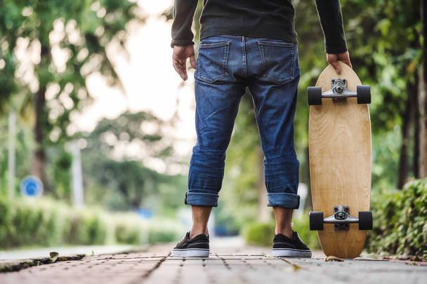  Asian man holding skate board in outdoor Park when sunrise time over photo blur of unrecognized people running, extream sport, healthy and exercise, fashion in covid19 concept - Foto, imagen