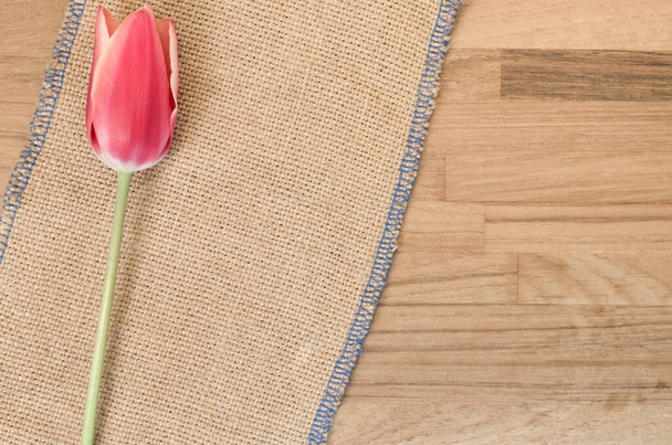 An overhead shot of a pink tulip flower against  burlap cloth on wooden table with space for your text - Фото, зображення