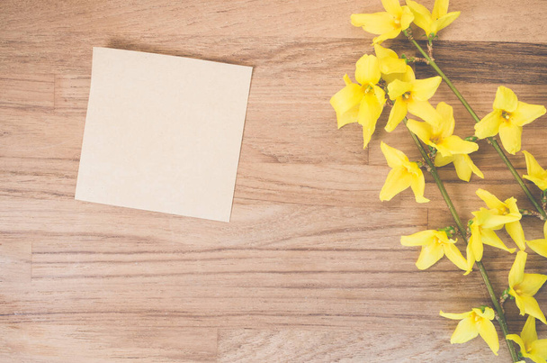 A high angle shot of forsythia flowers and a piece of paper on a wooden surface - Foto, immagini