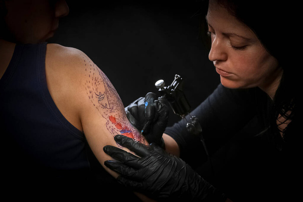 男性の腕にタトゥーを作る女性タトゥー アーティスト - 写真・画像