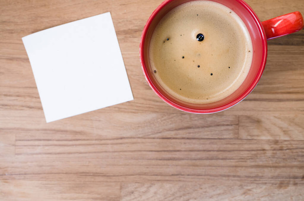 A high angle shot of a cup of coffee and a piece of paper on a wooden surface - Фото, изображение