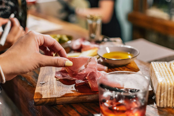 A female hand taking a piece of cured pork meat from a charcuterie board - Zdjęcie, obraz